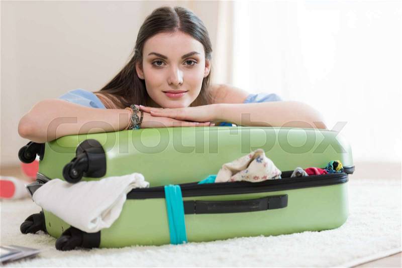 Beautiful young brunette woman packing suitcase and looking at camera, packing luggage concept, stock photo
