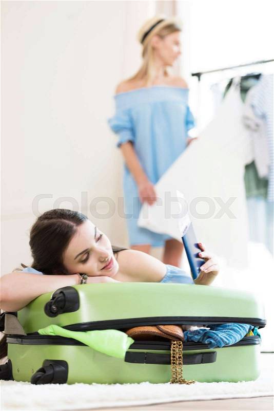 Smiling young woman leaning on suitcase and holding passports and tickets, packing luggage concept, stock photo