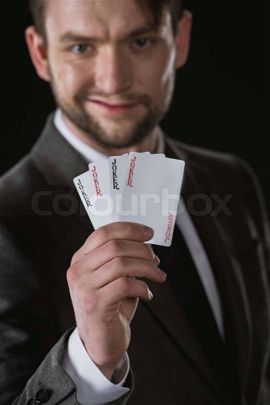 Businessman holding Joker cards in hand isolated on black, focus on foreground, stock photo
