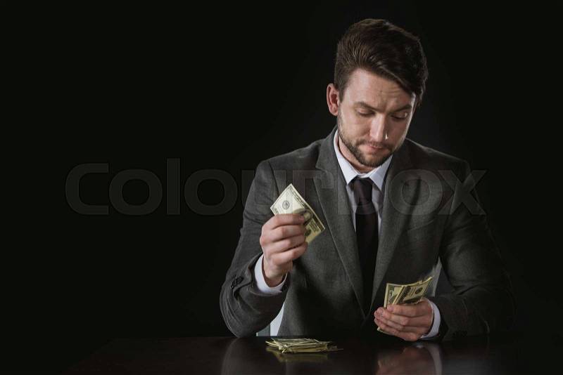 Portrait of businessman sitting at table and counting money isolated on black, stock photo