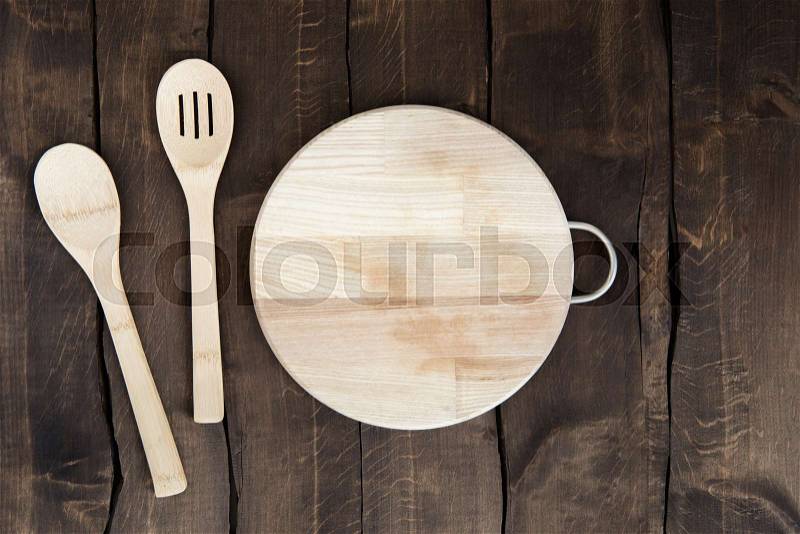 Overhead view of circular chopping board with kitchen utensils on wooden background, stock photo