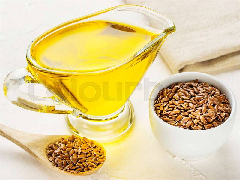Brown flax seeds in spoon and flaxseed oil in glass jug on trendy textured white concrete background. Flax oil is rich in omega-3 fatty acid, stock photo