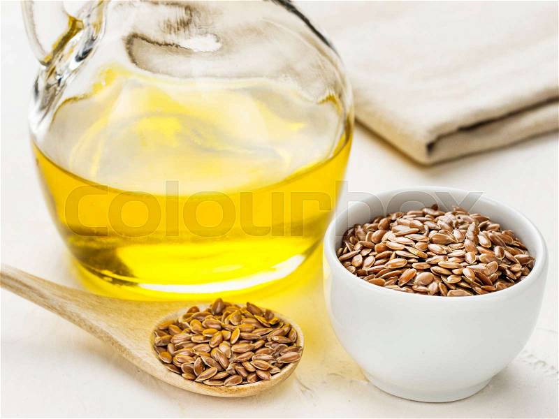 Brown flax seeds in spoon and flaxseed oil in glass bottle on trendy textured white concrete background. Flax oil is rich in omega-3 fatty acid, stock photo