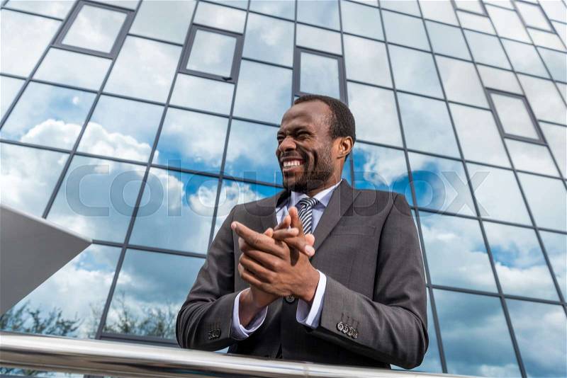 Portrait of successful african american businessman laughing and gesturing while standing at office building, stock photo