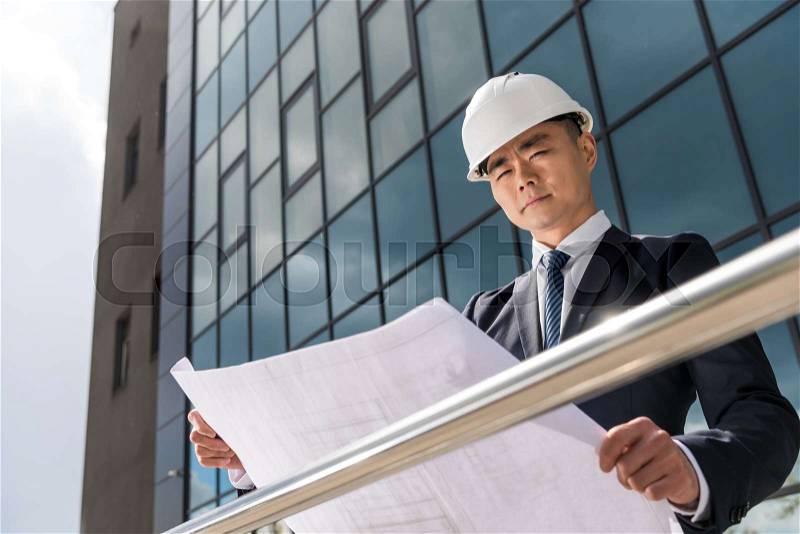 Portrait of serious professional architect in hard hat looking at blueprint, stock photo