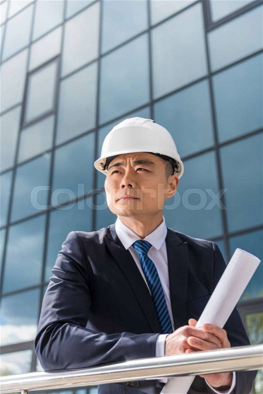 Portrait of pensive professional architect in hard hat holding blueprint, stock photo