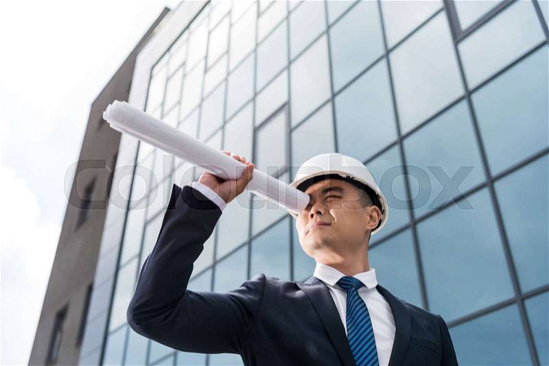 Portrait of professional architect in hard hat looking through blueprint in hand, stock photo