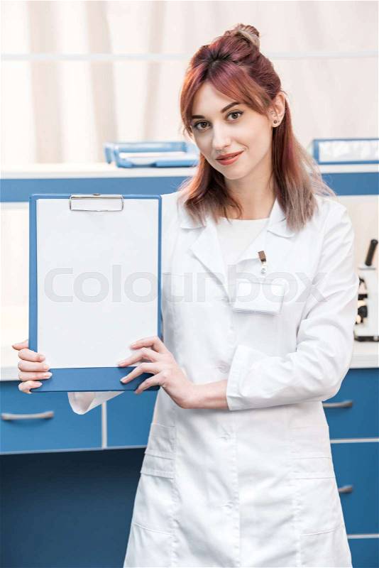 Young scientist in lab coat showing folder and looking at camera in chemical lab, stock photo