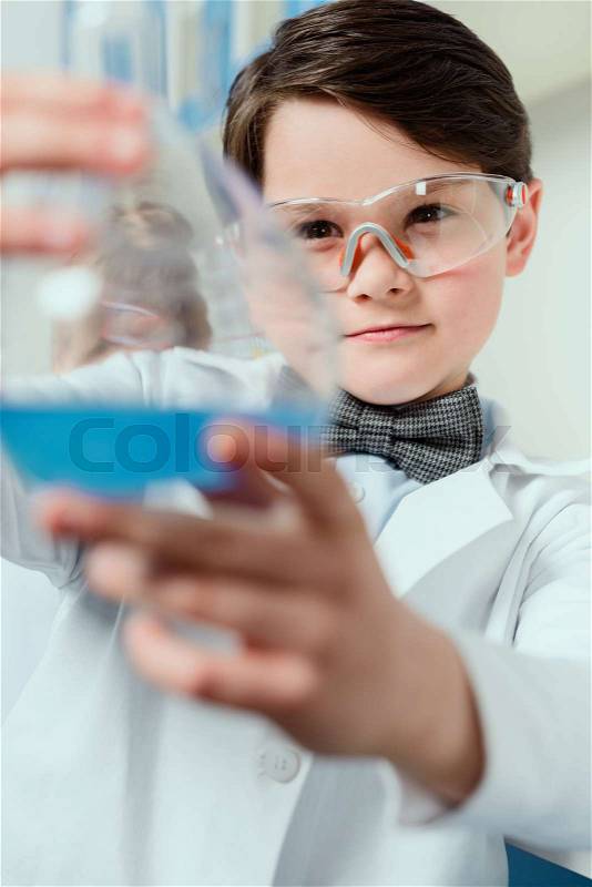 Schoolboy in goggles holding flask in chemical lab, science student concept, stock photo