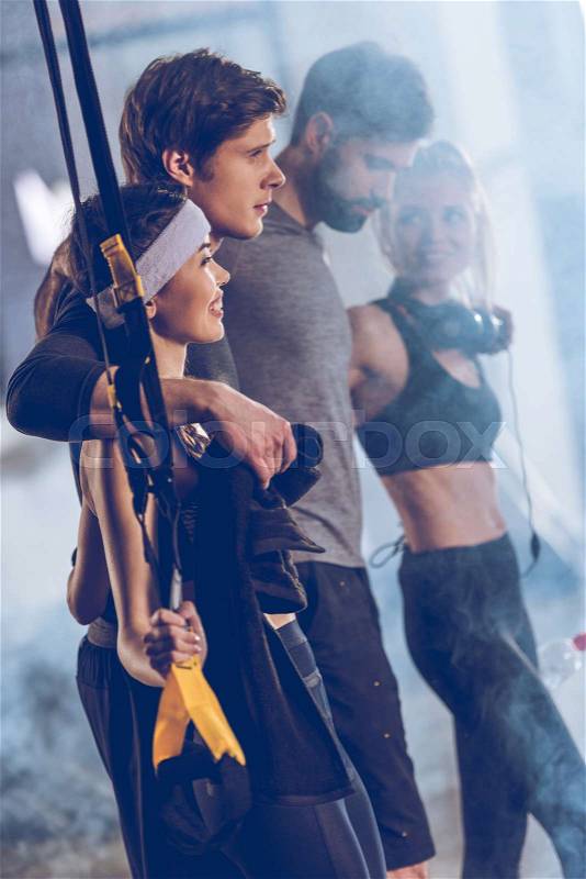 Side view of group of sportive people near trx equipment in gym, stock photo