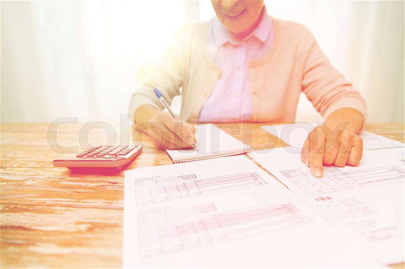 Business, savings, annuity insurance, age and people concept - close up of senior woman with papers or bills and calculator writing at home, stock photo