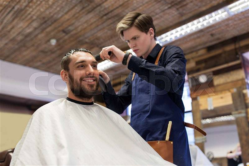 Grooming, hairstyle and people concept - man and barber or hairdresser with trimmer cutting hair at barbershop, stock photo