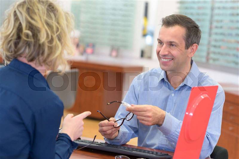 Attractive optician working with customer in his glasses shop, stock photo