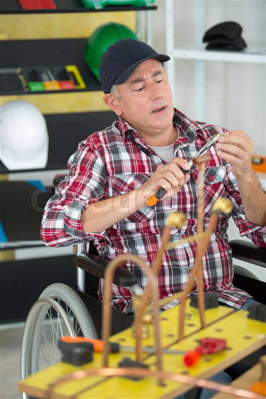 Disabled middle-age worker in wheelchair in a workshop, stock photo