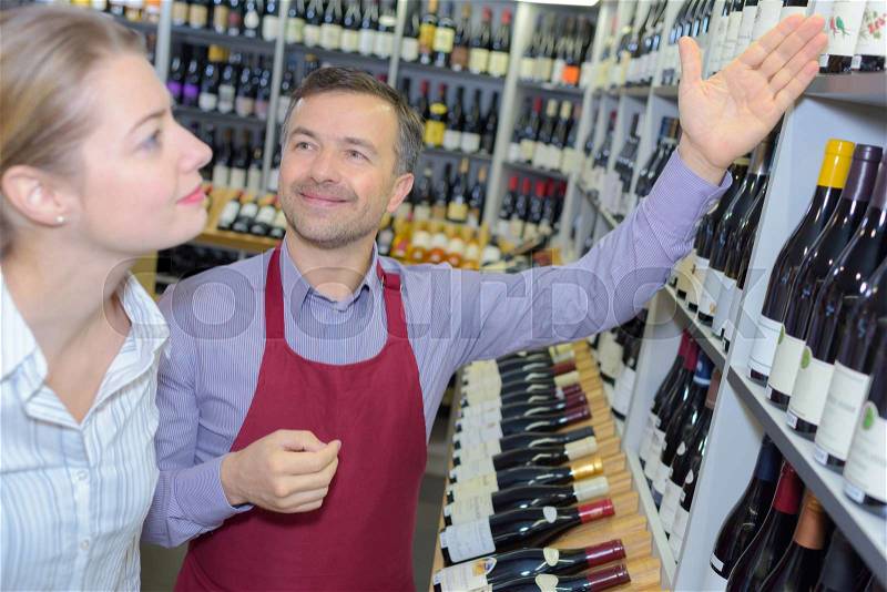 Shop assistant helps customer to choose wine in supermarket, stock photo