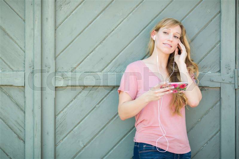 Outdoor Portrait of Young Adult Brown Eyed Woman Listening To Music with Earphones on Her Smart Phone, stock photo