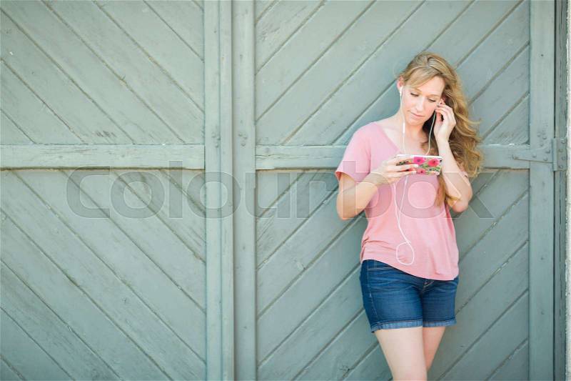 Outdoor Portrait of Young Adult Brown Eyed Woman Listening To Music with Earphones on Her Smart Phone, stock photo