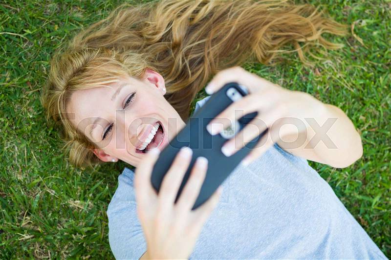 Young Adult Woman Laying in Grass Taking a Selfie with Her Smart Phone, stock photo