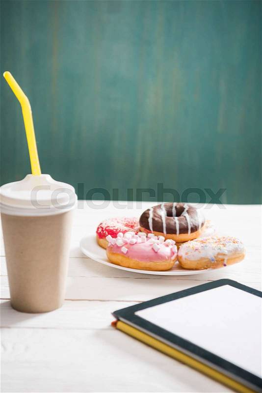 Unhealthy breakfast with coffee to go, plate of frosted donuts and digital tablet with white screen on wooden table. donuts and coffee background, stock photo