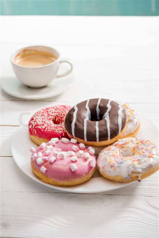 Plate full of donuts with colorful icing and cup of coffee for breakfast , stock photo