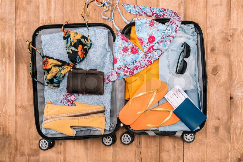 Top view of open luggage full of woman\'s clothes and other essential vacation items. Ready to summer vacation, stock photo