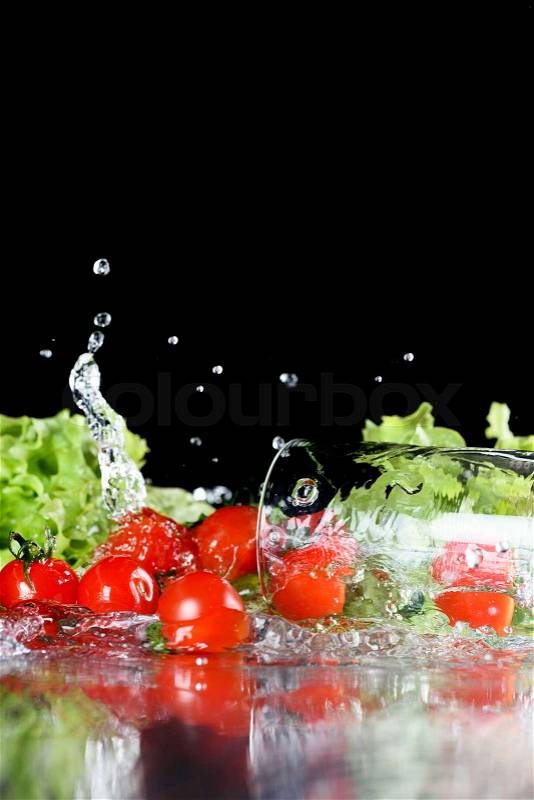Red fresh cherry tomatoes and green lettuce in water isolated on black, harvest vegetables and leafy vegetables concept, stock photo