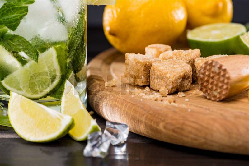 Close-up view of mojito cocktail in glass, crushed sugar, limes and ice cubes on table, cocktail drinks concept, stock photo