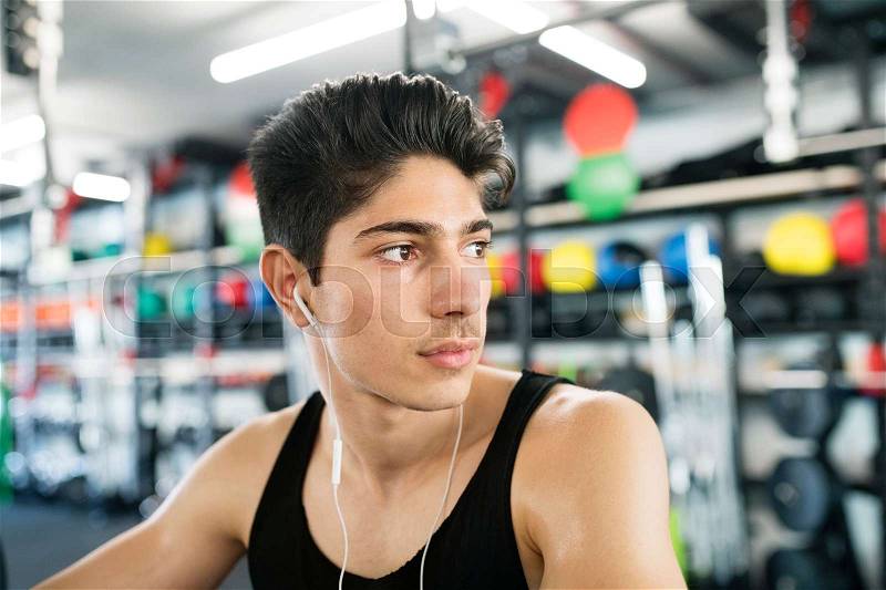 Hispanic fitness man in gym at the heavy barbell, resting, earphones in his ears, listening music, stock photo
