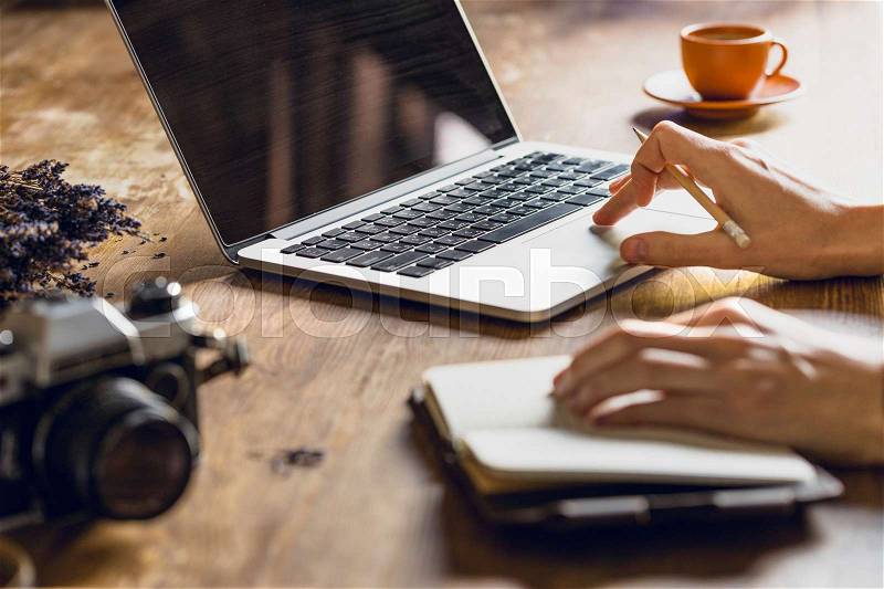 Person using laptop and diary at workspace with vintage photo camera, stock photo