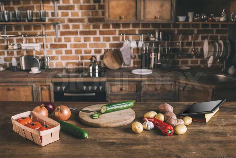 Kitchen table with variety of raw vegetables, chopping board and digital tablet ready for preparing breakfast , stock photo