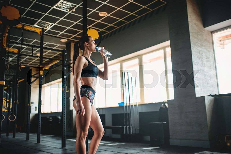 Attractive female athlete drink water after training in gym. Slim woman in fitness club, stock photo