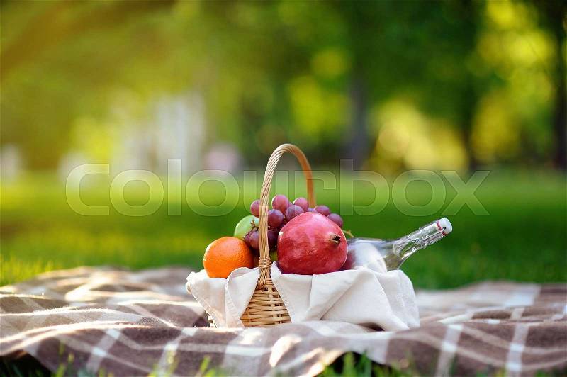 Picnic basket with fruits, food and water in the glass bottle. Outdoors leisure time for kids, family or dating couple. Sunny warm day in the summer park, stock photo