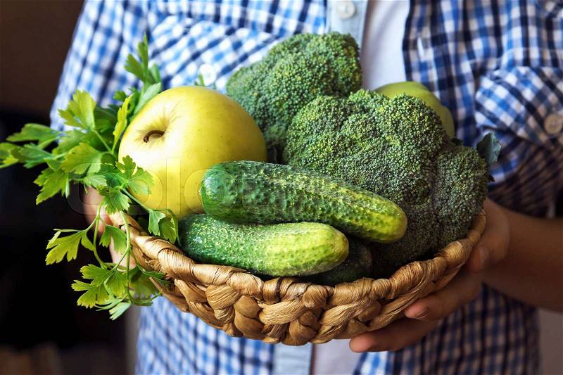 Person (hands) hold basket with organic green vegetables (broccoli, cucumbers, apple and parsley) - healthy organic detox diet vegan vegetarian raw eating concept, fresh ingredients for healthy food, stock photo