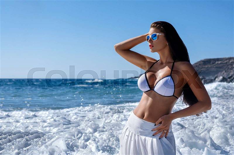 Beautiful brunette young woman wearing white bikini and skirt sunbathing in ocean. outdoor fashion shot. copy space, stock photo