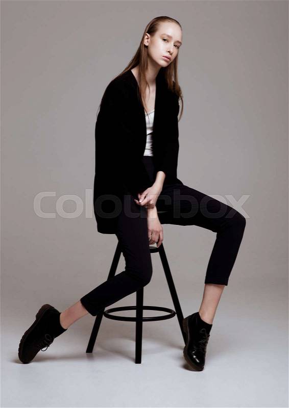 Model test portrait with young beautiful fashion model posing on grey background. Wearing black pants and jacket, stock photo