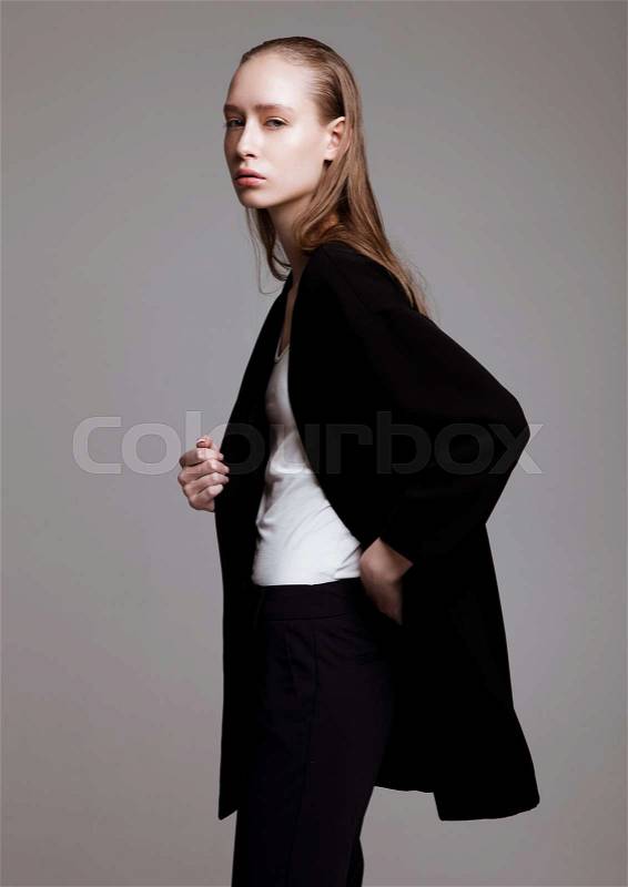 Model test portrait with young beautiful fashion model posing on grey background. Wearing black pants and jacket, stock photo