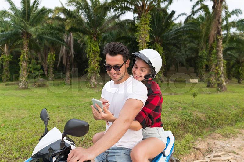 Couple Riding Motorbike, Young Man And Woman Using Cell Smart Phone Travel On Bike On Tropical Forest Road During Exotic Summer Holiday, stock photo