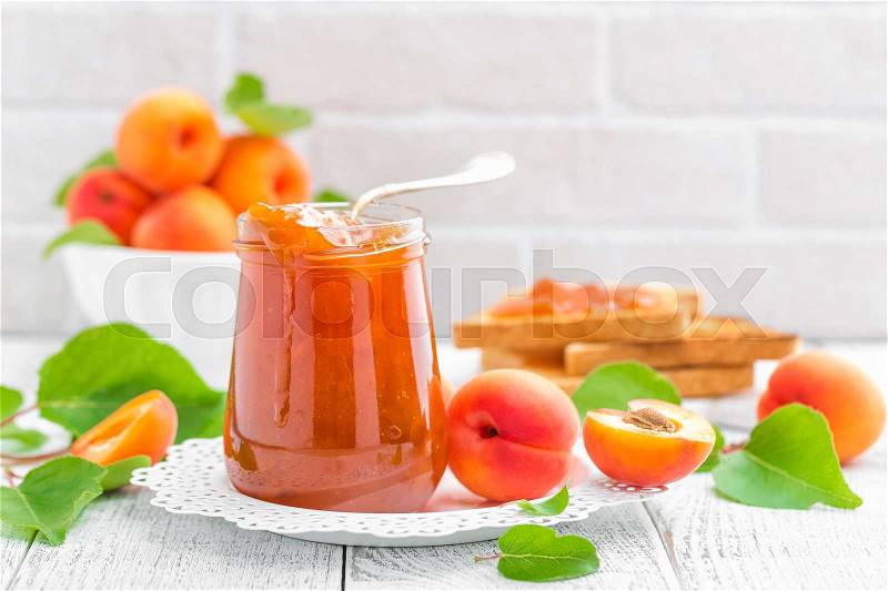 Apricot jam in a jar and fresh fruits with leaves on white wooden table, breakfast, stock photo