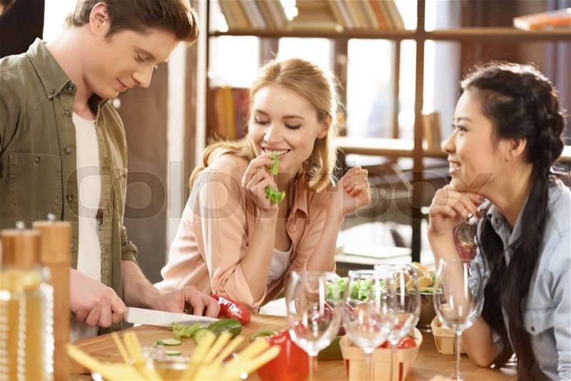 Young people partying, eating and drinking wine at home party, stock photo