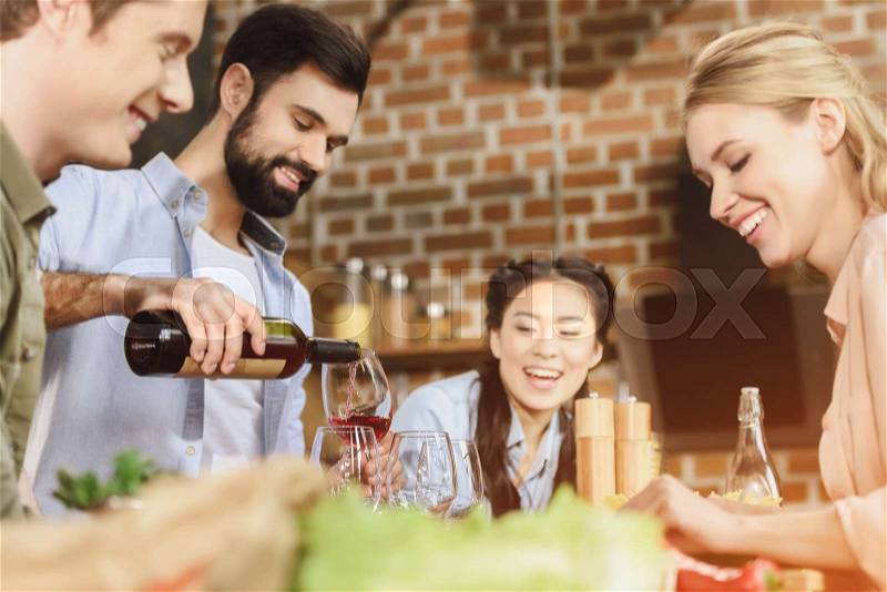 Young people partying at kitchen, having food, drinking wine at home party, stock photo