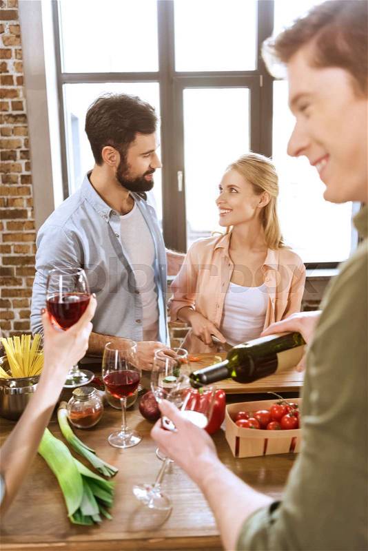 Young people partying at kitchen, having fun, drinking wine at home party, stock photo