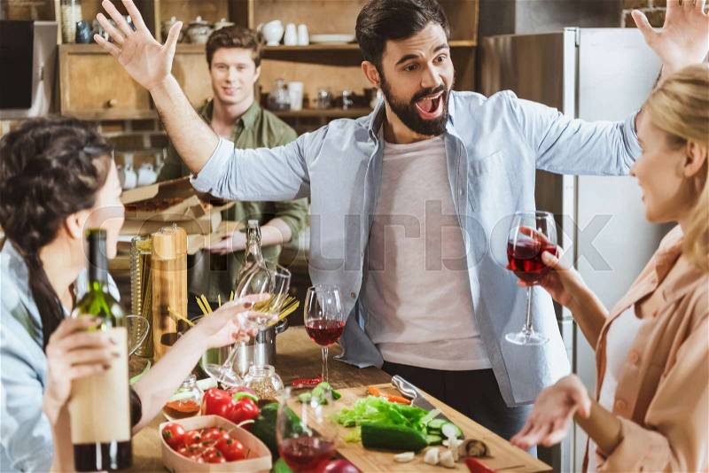 Young people partying at kitchen, drinking wine, having food at home party, stock photo