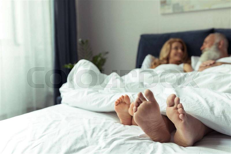 Close-up view of feet of happy mature couple resting together in bed , stock photo