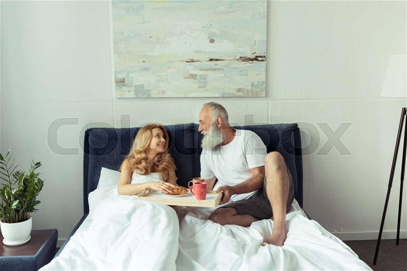 Happy wife and husband having breakfast in bed together, stock photo