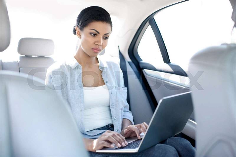 Concentrated african american woman working with laptop in taxi , stock photo