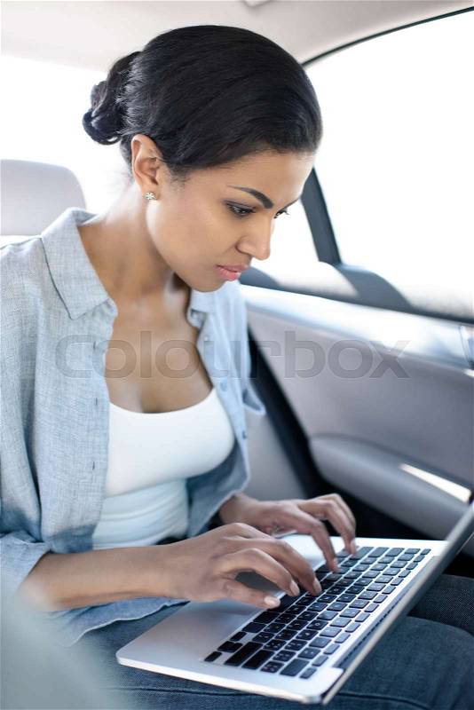 Concentrated african american woman working with laptop in taxi , stock photo