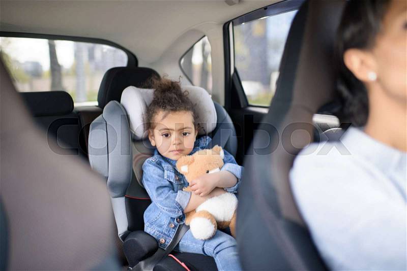 Little girl holding teddy bear while sitting in car, stock photo