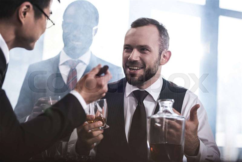 Multiethnic group of businessmen smoking and drinking whisky indoors, business team meeting, stock photo