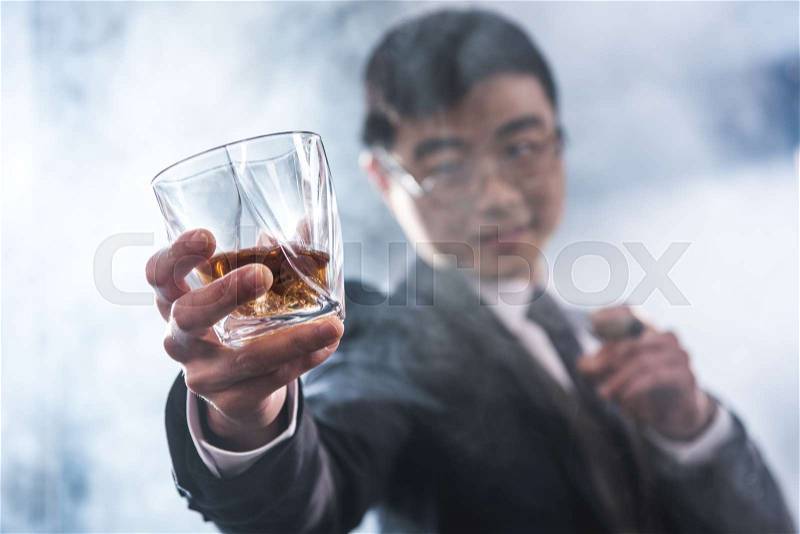 Close-up view of confident asian businessman drinking whiskey and smoking cigar, stock photo