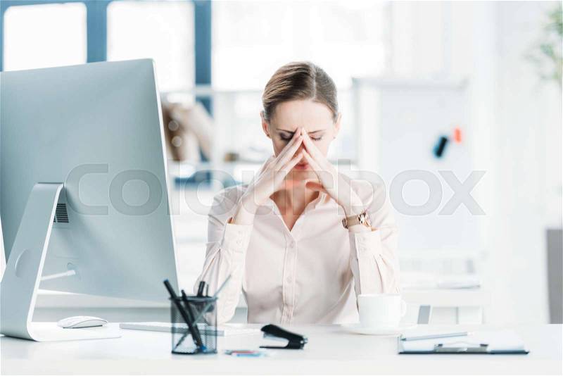 Young tired businesswoman sitting near computer at modern office, stock photo